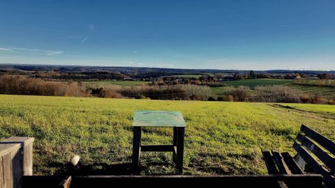 Eine weitläufige Landschaft mit grünen Feldern und sanften Hügeln. Im Vordergrund steht ein Tisch auf einer Anhöhe unter klarem Himmel.