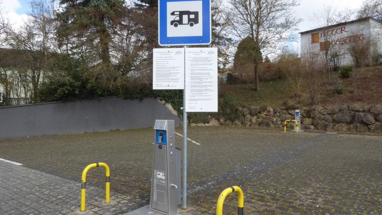 Een parkeerplaats voor campers met een informatiebord. Op de voorgrond staat een betaalderminal naast gele palen.