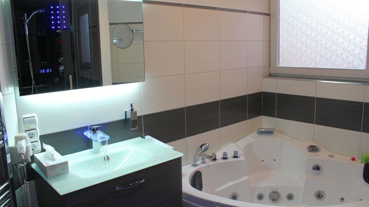 Ein modernes Badezimmer mit einer Whirlpool-Badewanne und einem Waschbecken aus Glas. Der Raum ist hell und gut beleuchtet, mit großen Fenstern und stylishen Fliesen.