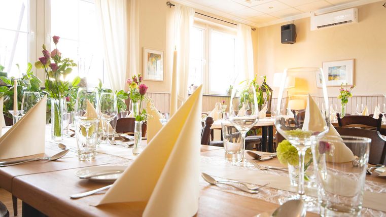 Ein gemütlicher Restaurantbereich mit schön gedeckten Tischen. Die Tischdekoration umfasst Blumen und Gläser, die eine einladende Atmosphäre schaffen.