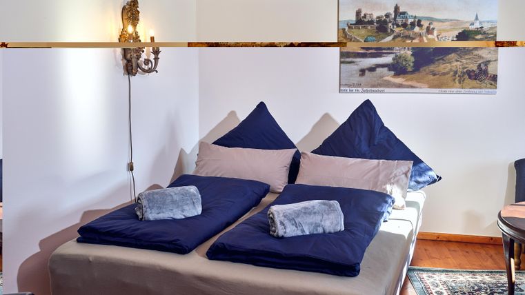 A cozy bedroom with a double bed and blue pillows. On the wall hangs a picture of a landscape.