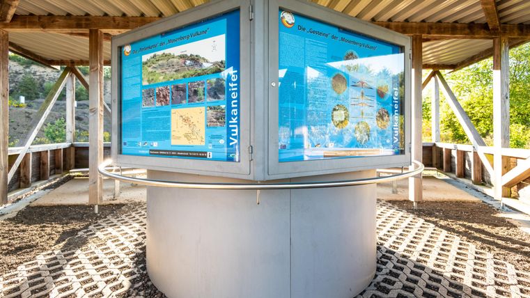 Ein Informationspavilion über Vulkane mit mehreren Tafeln und Bildern. Der Pavillon steht in einer natürlichen Umgebung.