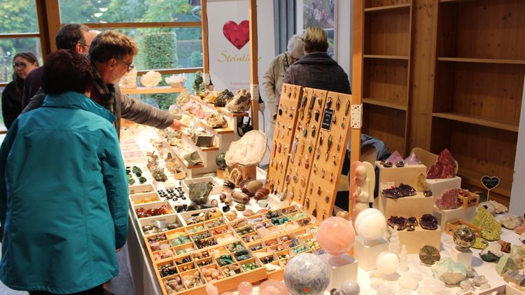 Een marktkraam met verschillende kristallen en sieraden. Mensen bekijken de etalages en interageren met elkaar.