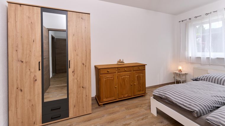 Ein modernes Schlafzimmer mit einem großen Kleiderschrank und einem Holzschrank. Der Raum hat helle Wände, ein gemütliches Bett und viel Tageslicht.