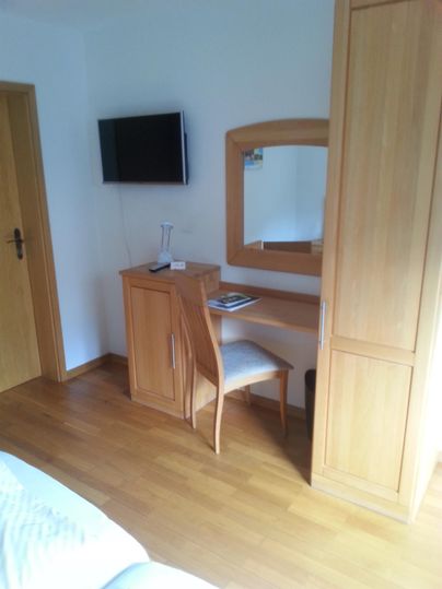 A cozy room with a table, a chair, and a mirror. A television is hanging on the wall.