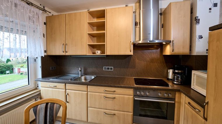 Eine moderne Küche aus Holz mit hellen Schränken und Edelstahlgeräten. Der Raum hat ein großes Fenster, das Licht hereinlässt.