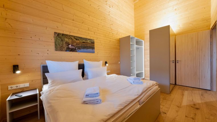 Ein gemütliches Schlafzimmer mit Holzwänden und einem großen Bett. Auf dem Bett liegen frische Handtücher und es gibt einen modernen Schrank.
