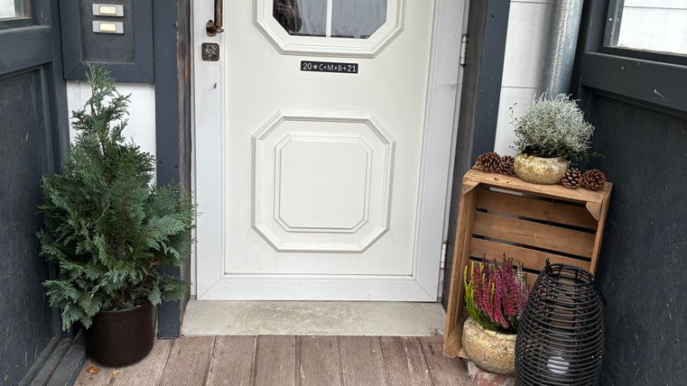 Eine einladende Eingangstür mit einem gemütlichen Fußmatte und einer Dekoration aus Pflanzen. Der Schriftzug "Wie schön, dass du da bist" vermittelt ein herzliches Willkommen.