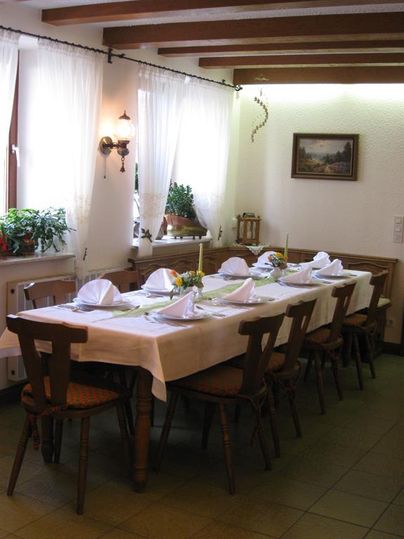 Ein eleganter Essbereich mit einem langen Tisch, der für ein Essen gedeckt ist. Große Fenster lassen viel Licht herein und verleihen dem Raum eine einladende Atmosphäre.