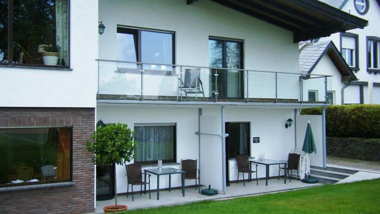 Een modern gebouw met een balkon en tuinmeubels in de tuin. De gevel is licht geschilderd en omringd door groen gras.