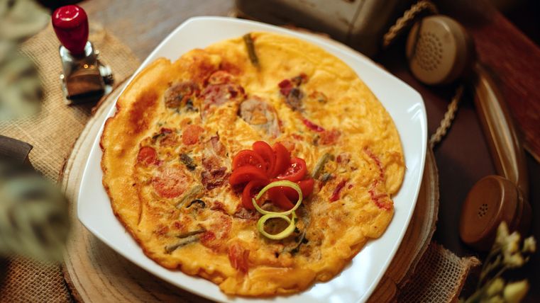 A delicious omelet with fresh vegetables and decorative ingredients. The meal is served on a rustic table.