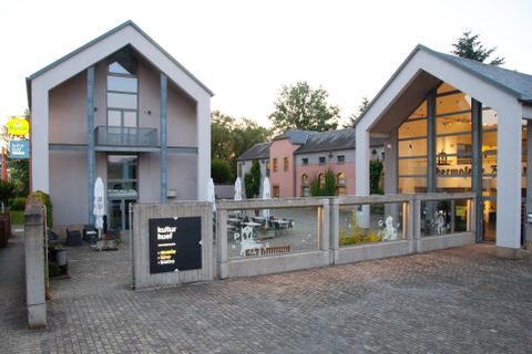 Ein modernes Gebäude mit zwei separaten Eingängen und großen Fenstern. Der Außenbereich ist mit Tischen und Sonnenschirmen ausgestattet, ideal für eine entspannte Atmosphäre.