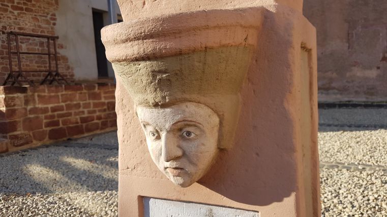 Een kunstzinnig reliëf van een gezicht op een staande voet. De sculptuur heeft een interessante vorm en bevindt zich in een stenige omgeving.