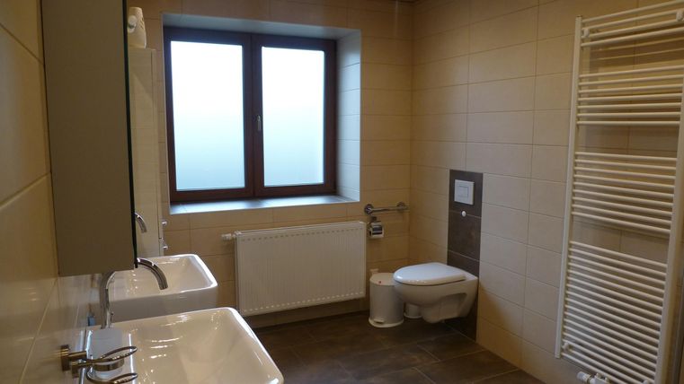 Ein modernes Badezimmer mit zwei Waschbecken, einer Toilette und einem Heizkörper. Das Fenster lässt natürliches Licht herein.