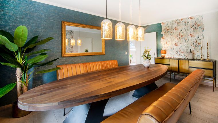 Een stijlvolle eetruimte met een ovale houten tafel en gezellige banken. De wanden zijn in zachte kleuren gehouden en er zijn moderne verlichtingsarmaturen.