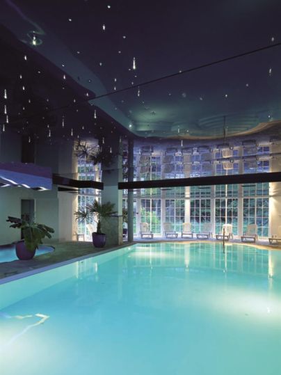 An elegant indoor pool with clear, blue water. The ceiling is adorned with sparkling lights and large windows provide plenty of daylight.