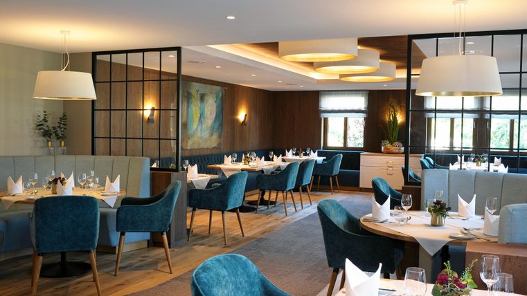 Ein elegantes Restaurant mit blauen Stühlen und festlich gedeckten Tischen. Die Beleuchtung ist warm und einladend.