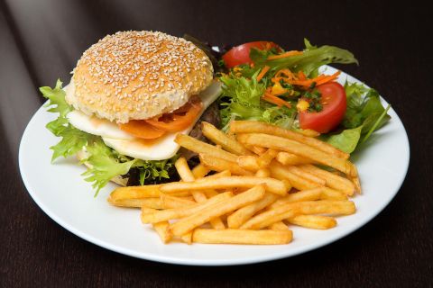 <p>A juicy burger topped with cheese, tomatoes, and lettuce, on a white plate. Next to it are French fries and some lettuce leaves and tomatoes.</p>