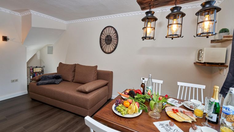 A cozy living and dining room with a sofa and a dining table. Fresh fruit and drinks are arranged on the table.