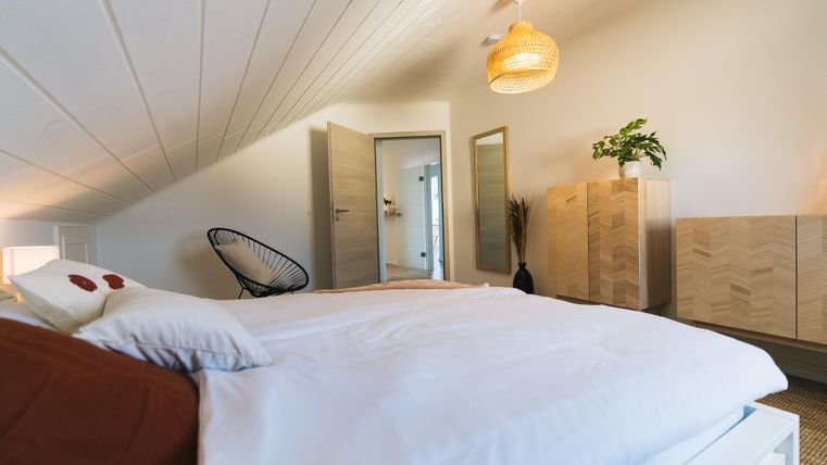 Een gezellige slaapkamer met een groot bed en een moderne inrichting. De muren zijn licht, en een houten plank en planten zorgen voor een aangename sfeer.