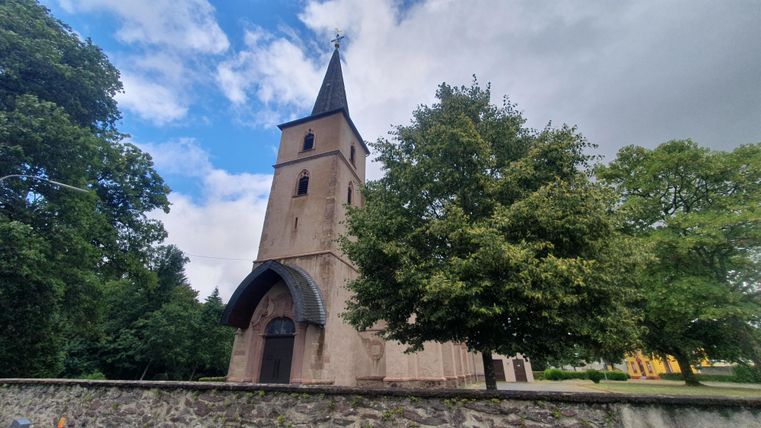 Een oude kerk met een hoge toren en klassieke architectonische details. Omringd door bomen en een heldere lucht.