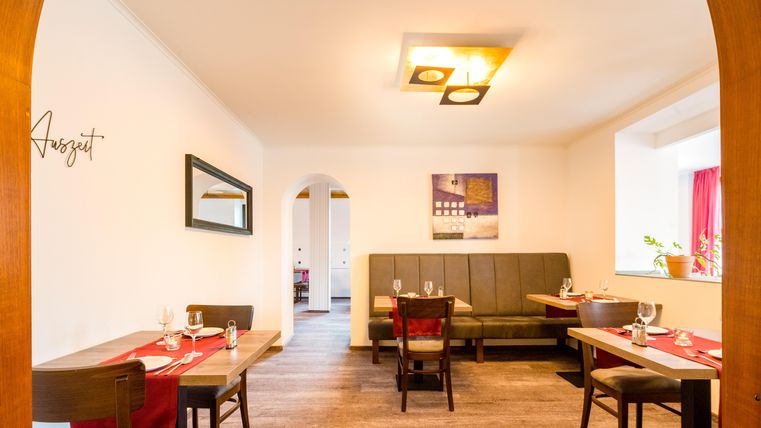 A cozy restaurant with wooden chairs and tables. The walls are bright and friendly, and there is elegant lighting.