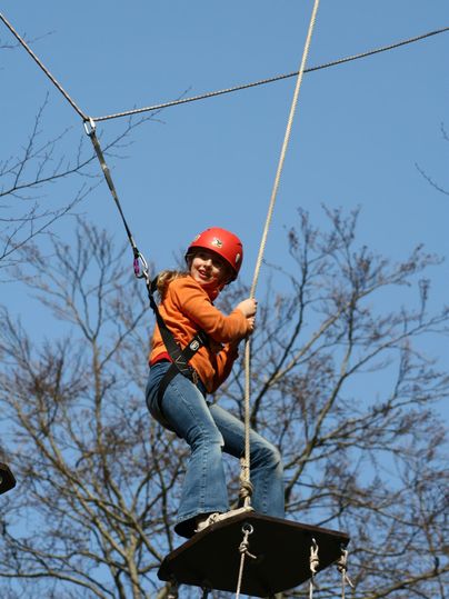 A girl in a red helmet is balancing on a tightrope. The sky is clear and blue.