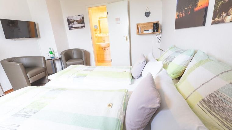 A cozy room with two beds and pretty decoration. In the background, a television and a bathroom can be seen.