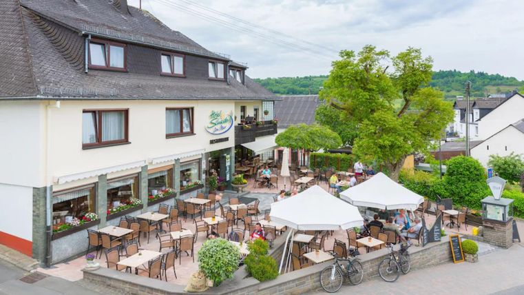 Een gezellig café met een terras en veel tafels buiten. Op de achtergrond zijn bomen en een rustige omgeving te zien.