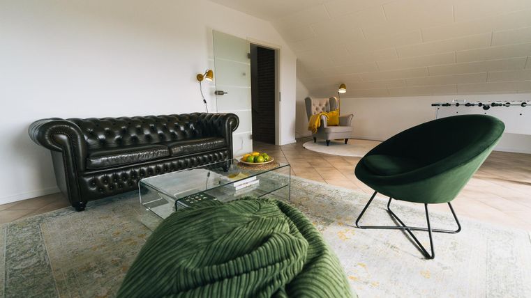 Een moderne woonkamer met een elegant, zwartbank en een groene fauteuil. De kamer heeft een lichte en vriendelijke uitstraling met een neutrale kleur.