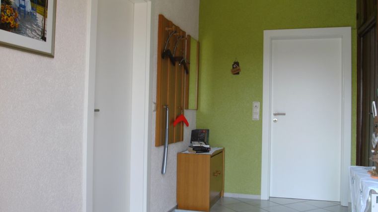 Ein heller Flur mit grünem Wandanstrich und hellen Fliesen. An der Wand hängen Schlüssel und ein kleiner Tisch steht neben der Tür.