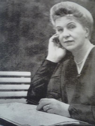 Eine nachdenkliche Frau sitzt auf einer Bank und betrachtet ein Buch. Sie trägt ein schlichtes, elegantes Outfit und hat eine zurückhaltende Pose.