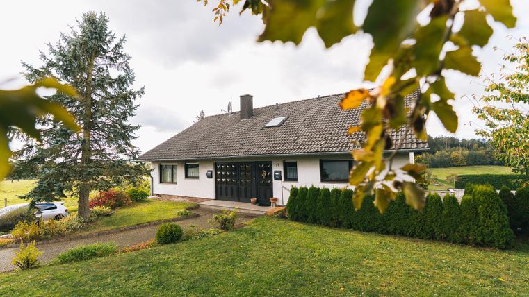 Een mooie eengezinswoning omgeven door groen en bomen. De gevel is licht met een donkere voordeur.