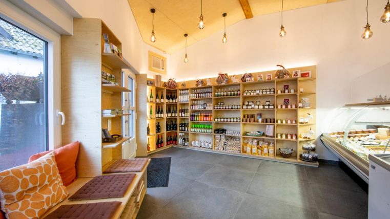 Ein einladendes Geschäft mit hellen Regalen, die eine Vielzahl von Lebensmitteln und Getränken präsentieren. Auf der Seite befindet sich ein gemütlicher Sitzbereich mit Kissen.