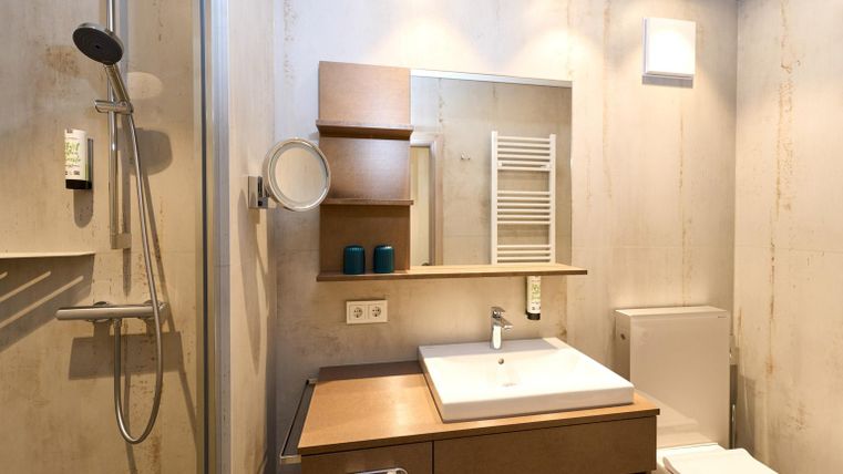 Een moderne badkamer met een douche en een houten wastafel. Er is een grote spiegel en een praktische opbergplek.