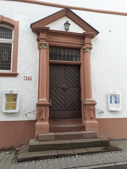 An old front door with elegant columns and a chandelier. The house has a white facade and is surrounded by stone steps.