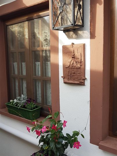 Eine schöne Hausfassade mit einem traditionellen Laternenlicht. Vor dem Fenster steht ein Blumentopf mit bunten Blumen.