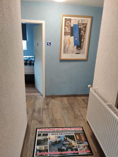 A bright hallway with blue walls and a piece of artwork on the wall. A striking carpet is on the floor.