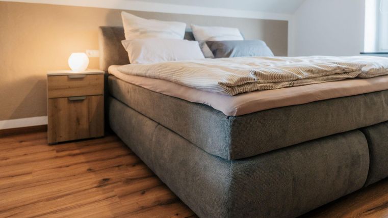 Ein modernes Schlafzimmer mit einem großen Bett und weichen Kissen. Neben dem Bett steht ein Nachttisch mit einer sanften Lampe.