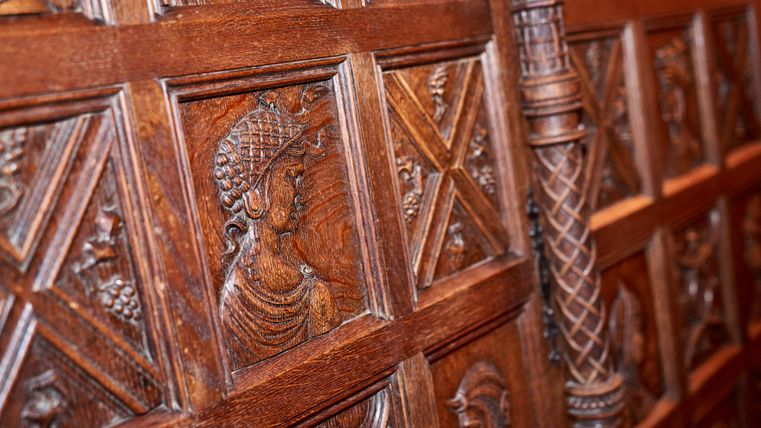 An artistically carved wooden wall with detailed reliefs of figures. The carvings depict historical or mythological motifs.