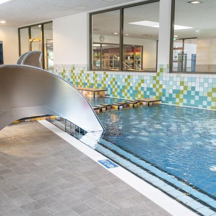 Ein moderner Innenpool mit einer Rutsche und farbenfrohen Fliesen. Das Wasser ist klar und der Bereich ist gut beleuchtet.