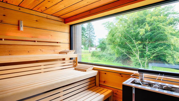 Moderne Sauna mit Holzverkleidung, Bänken und großem Fenster mit Blick auf grüne Natur.