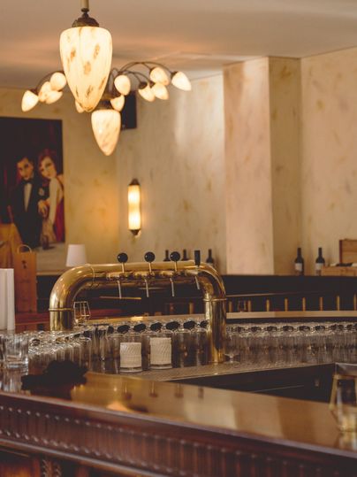 Een stijlvolle bar met een glanzende tapkraan en een rij glazen. Aan de muren zijn mooie lampen en een schilderij te zien.