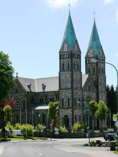 Eine beeindruckende Kirche mit zwei Türmen und grünen Dächern. Umgeben von Bäumen und einer ruhigen Straße.
