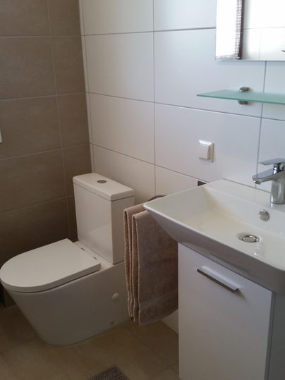 Ein modernes Badezimmer mit einer weißen Toilette und einem Waschbecken. An der Wand hängen ein Handtuch und es gibt einen kleinen Fenster mit Tageslicht.