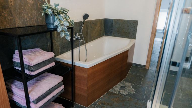 Ein modernes Badezimmer mit einer eleganten Badewanne und einer dekorativen Pflanze. Neben der Badewanne sind ordentlich gefaltete Handtücher auf einem Regal angeordnet.