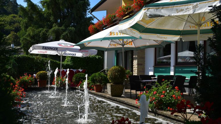 Ein schöner Außenbereich mit Brunnenskulpturen und blühenden Pflanzen. Sonnenschirme bieten Schatten für die Gäste.