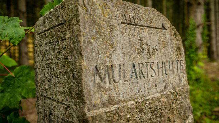 A stone signpost with the inscription "MULARTHÜTTE". Surrounded by trees and greenery.