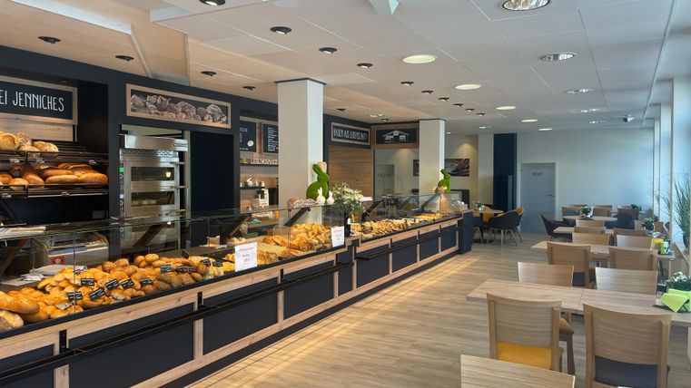 Een uitnodigend café met een grote selectie aan verse gebakjes. Helle tafels en stoelen creëren een aangename sfeer.