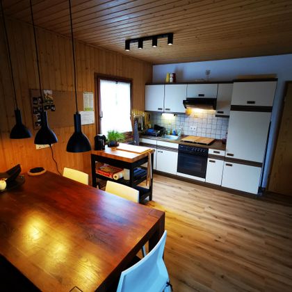 Een moderne keuken met houten plafonds en lichte meubels. Het eetgedeelte is eenvoudig ingericht met een grote tafel en stoelen.